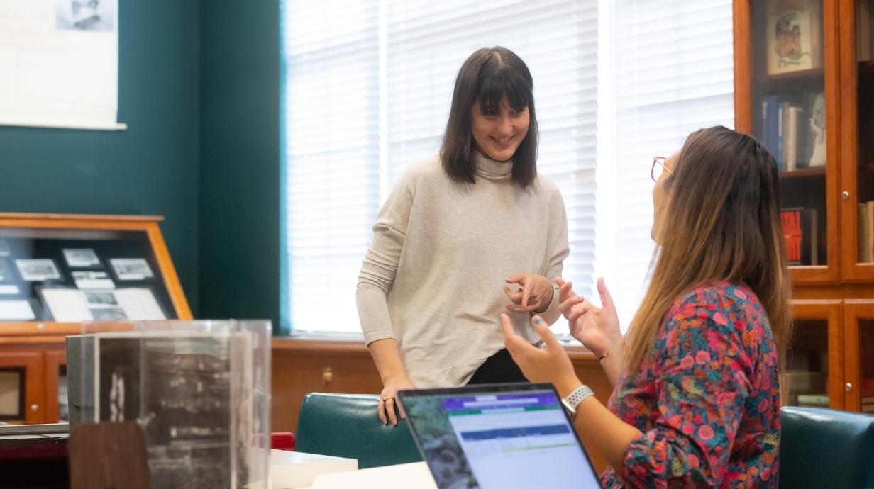 Two graduate students speaking in a library.