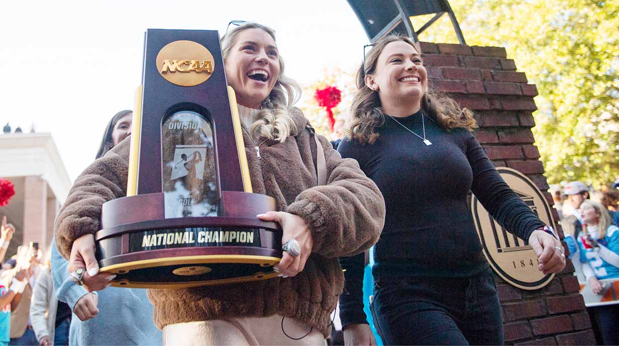 The Ole Miss Women's Golf Team carries their National Championship trophy down the Walk of Champions through the Grove.