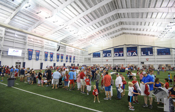 Inside of the Olivia and Archie Manning Athletics Performance Center during a fan event. Lots of people are on the field. The dramatic ceiling is featured prominently.