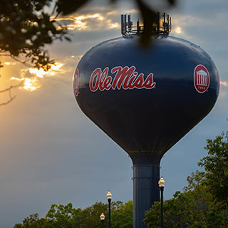 A powder blue water tower with an emblazoned "Ole Miss" logo at sunset