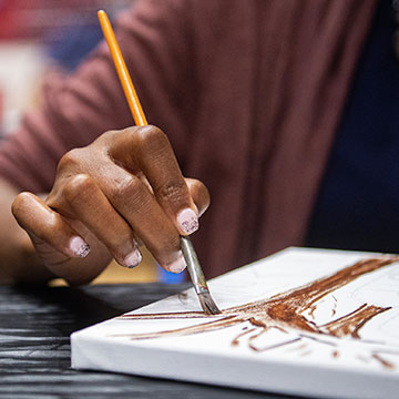 A hand with fingernail polish paints an image