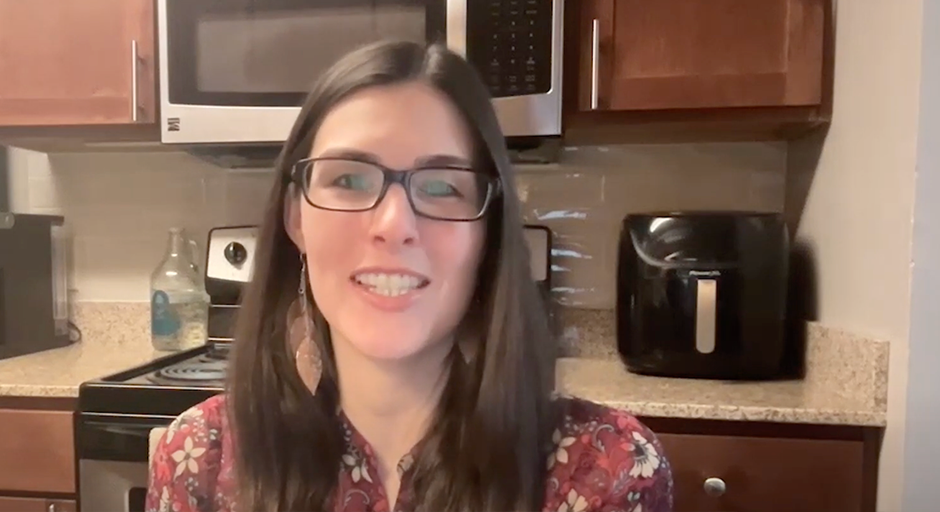 woman with glasses sits in kitchen smiling