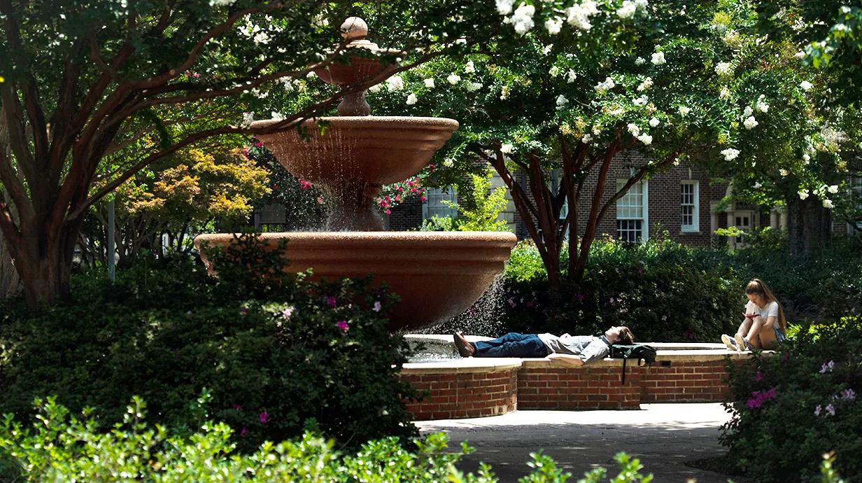 Students near the Phi Mu fountain. One laying down relaxing, the other one sitting up and looking down.