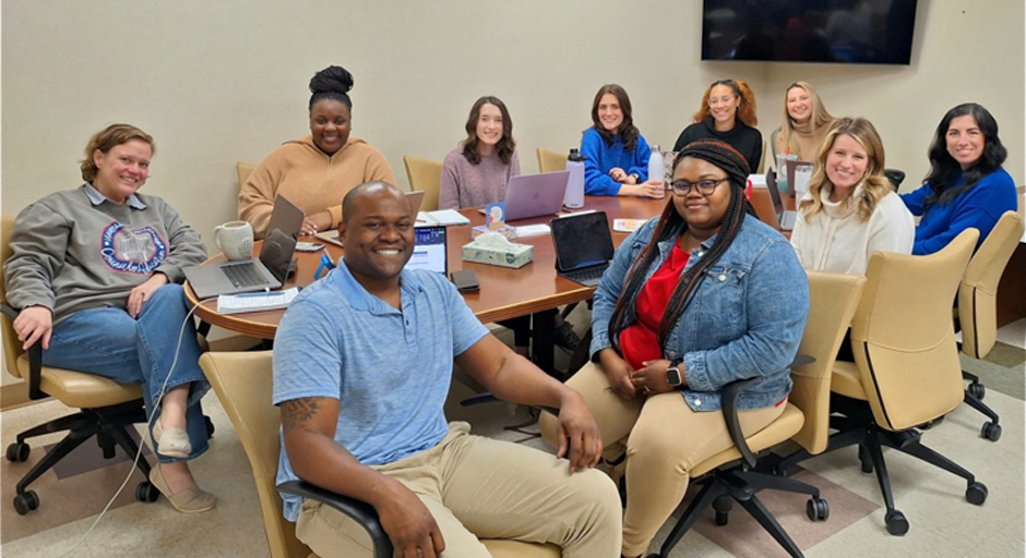 faculty and staff gathered around a conference table smiling 