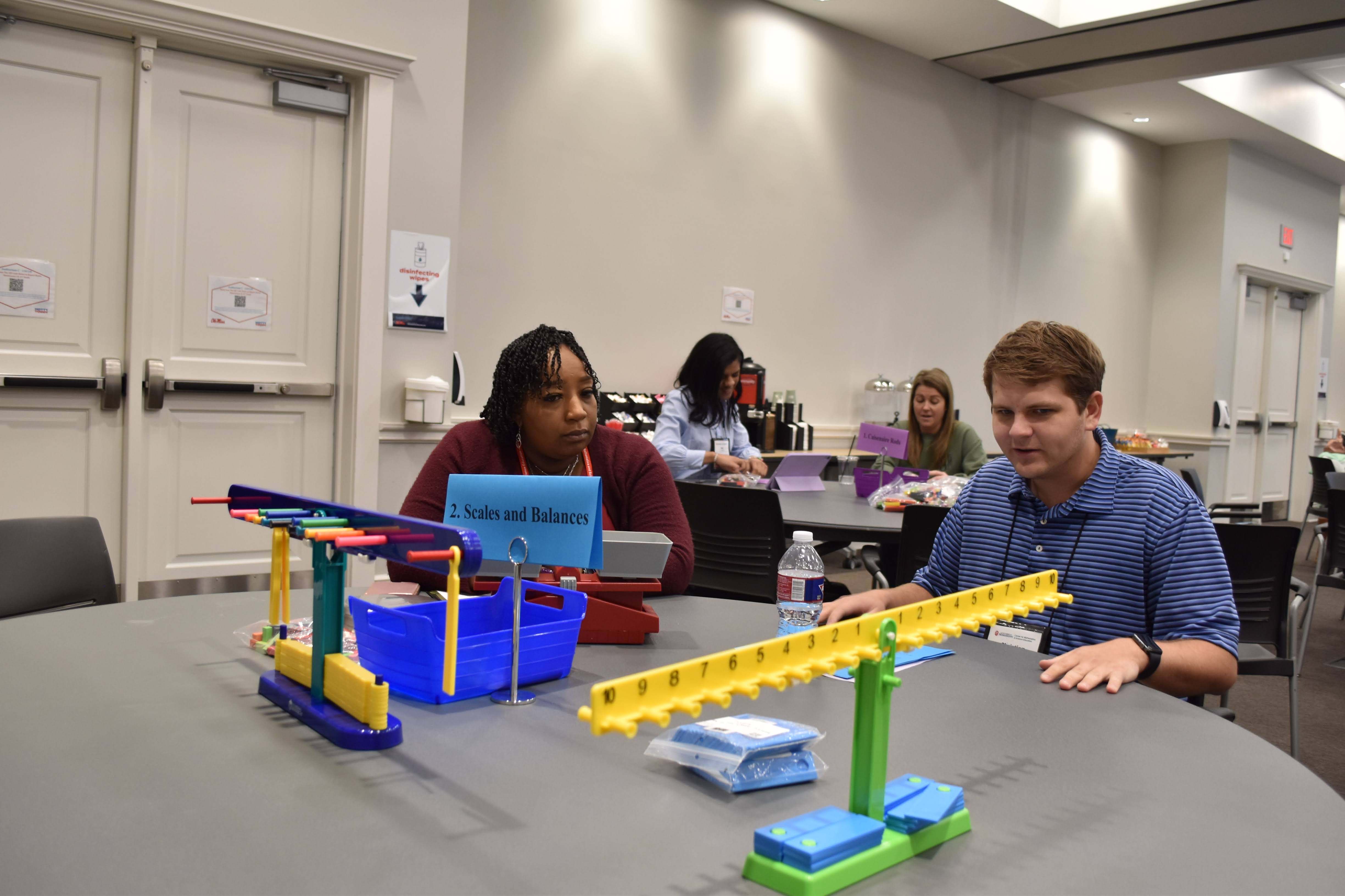 Two teachers work with a balance scale model.