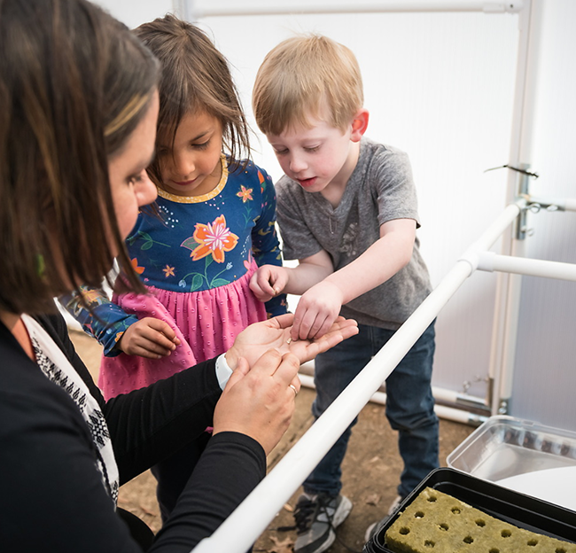 a teacher shows students how to plant seeds in the greenhouse