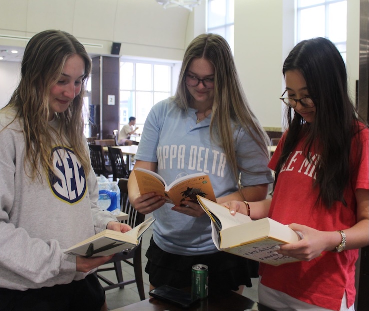 three female students hold a book in their hands