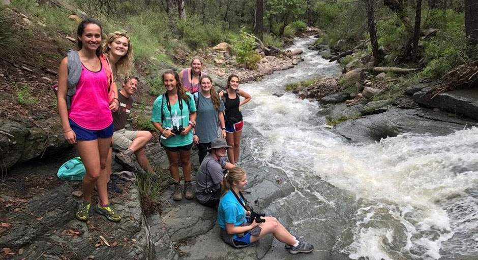 students sitting on rocks next to a small river