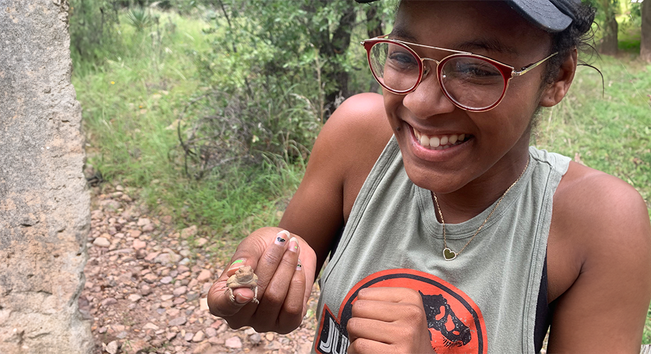 female student holds up a lizard while smiling