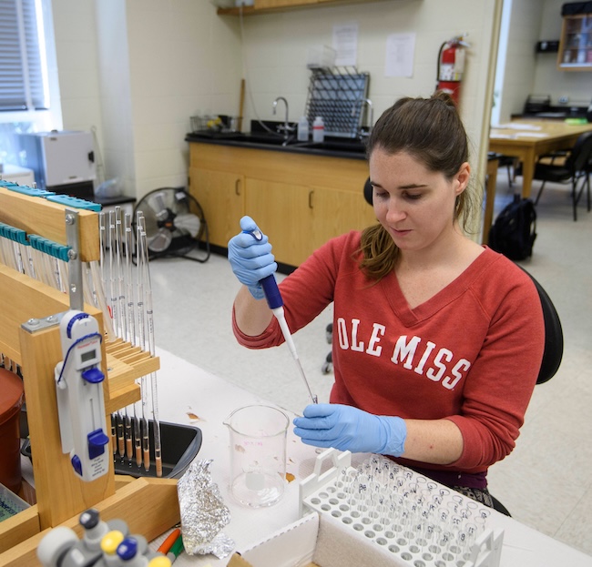 female graduate student wearing gloves and putting liquid in a test tube