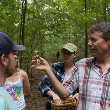 Professor holding a mushroom with students around him.