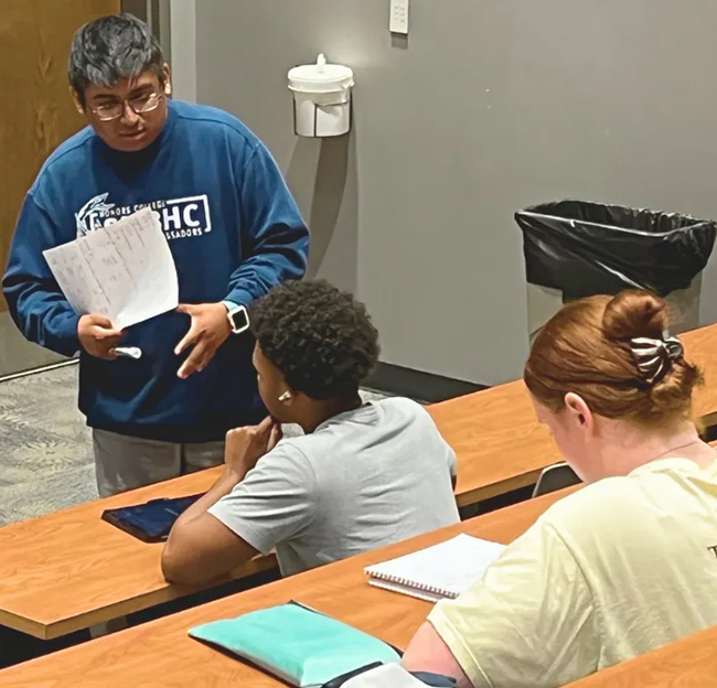 male student standing in front of other students and talking