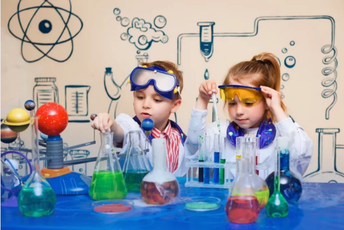 two children in lab coats and safety glasses using beakers and other lab equipment