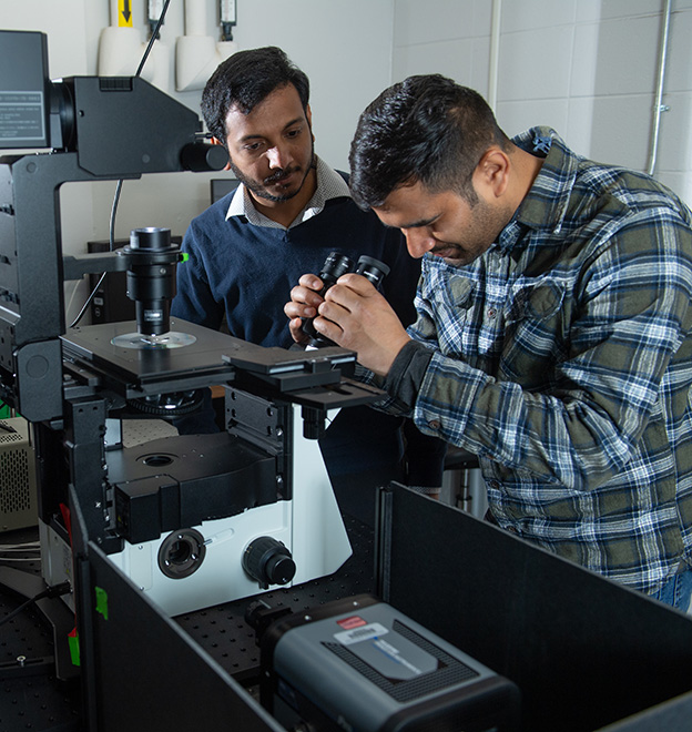 two male graduate students looking through a microscope