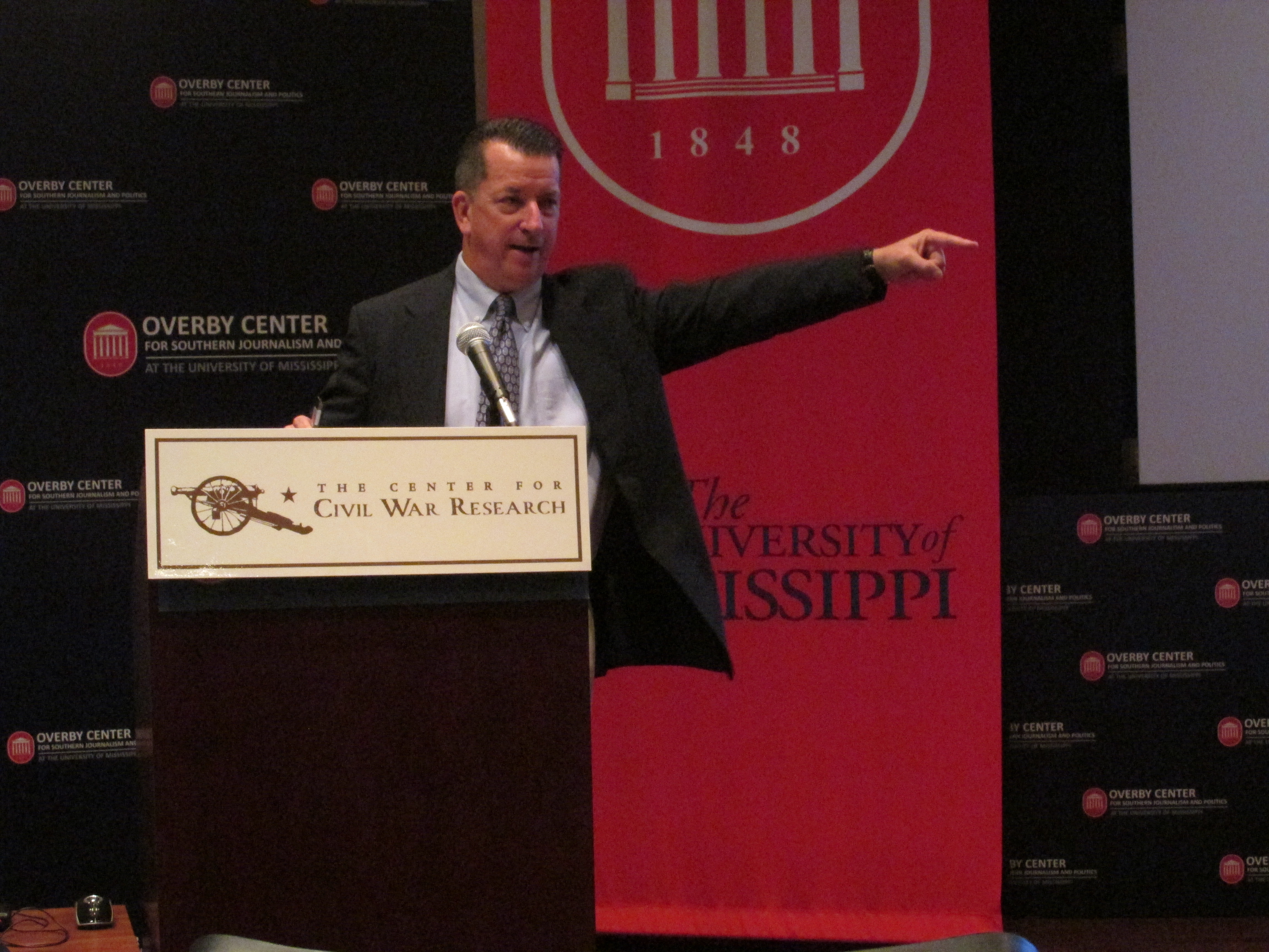 a man stands behind a podium and gestures while speaking