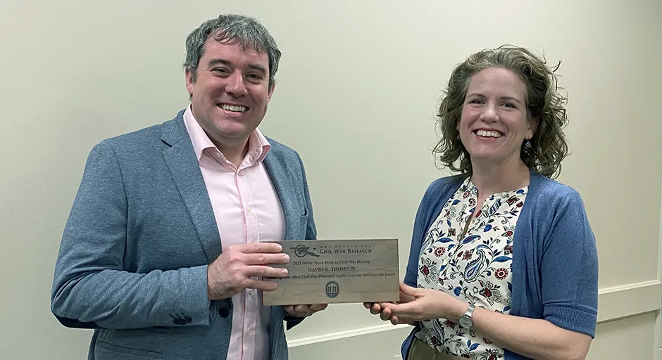 Man and woman smiling at the camera holding a plaque.