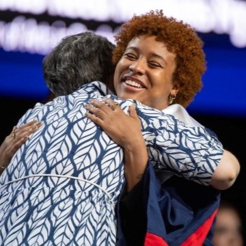 student in graduation robes and faculty member hugging on stage at honors college ceremony