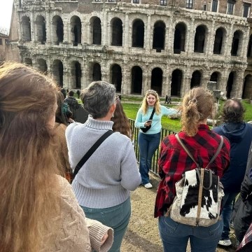 student making a presentation to a small group of people while standing in front of an ancient site in Rome