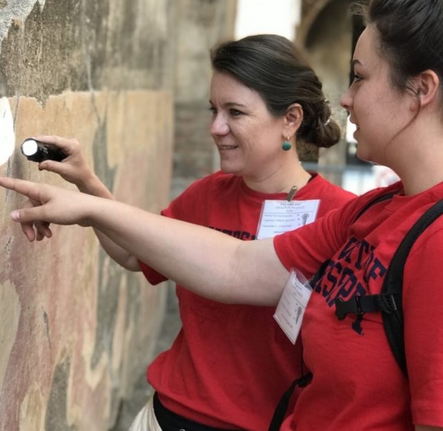 image of two women shining a light at ancient graffiti on a wall.