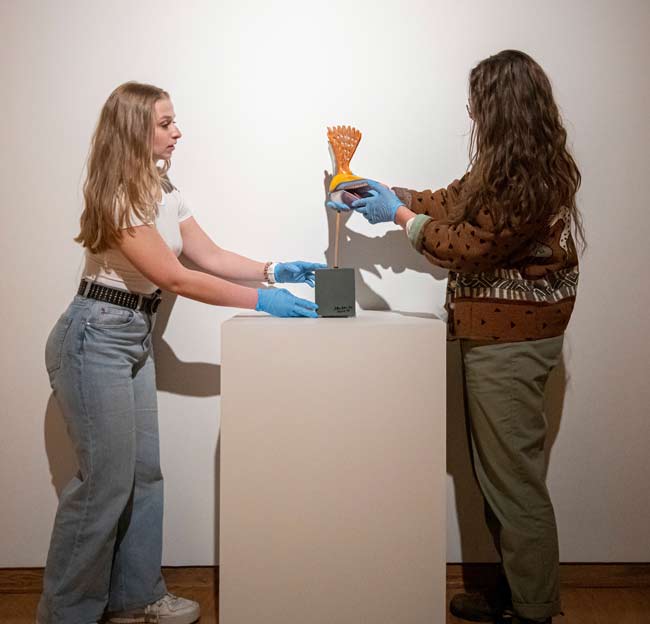 Two women arranging a sculpture in a gallery.