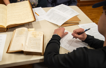 person sitting at a table with old books and papers scattered around them