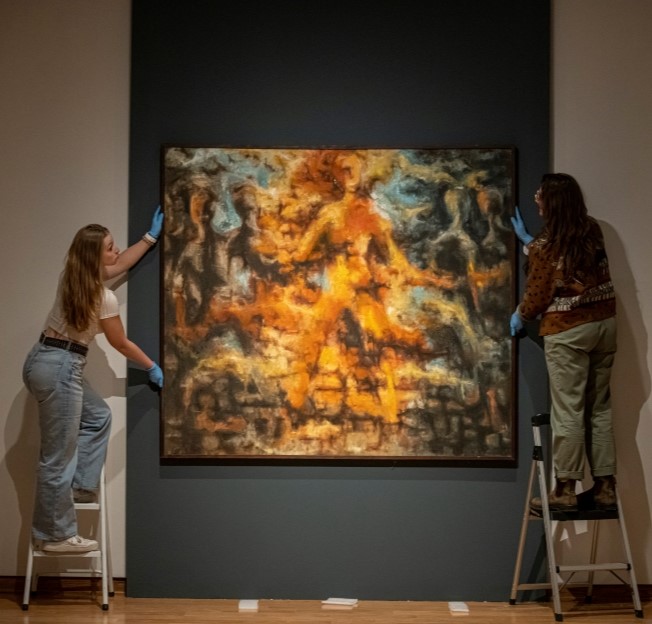 image of two students hanging a large painting on the museum wall