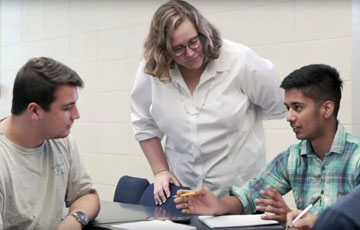 professor standing over two students who work at a table