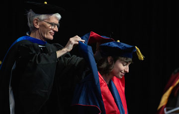 male professor in robes hooding a graduate female student