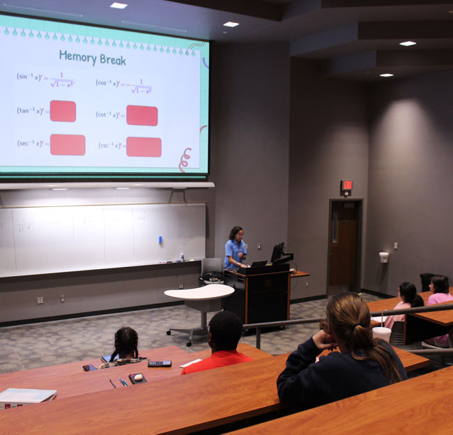 female tutor standing at podium in front of students and talking