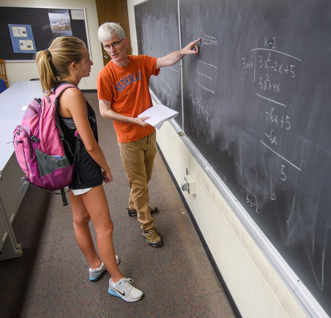 male professor pointing to a chalk board and talking with a female student