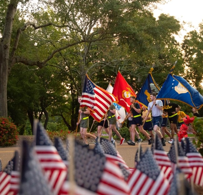 military cadets jogging down the road while carrying flags for 911 service