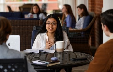 a small group of students seats in outside lounge furniture on a covered porch