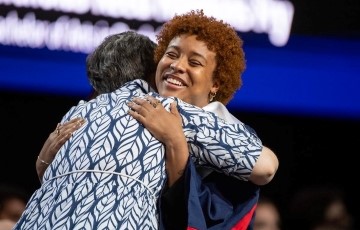 image of a student in graduation robes smiling and hugging a professor while on a graduation stage