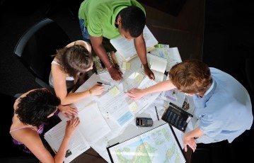 image of students gathered around a table with lots of papers