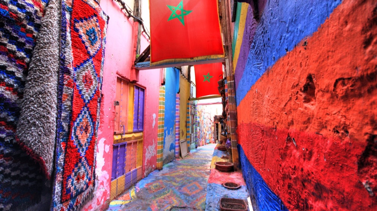 image of a colorful alleyway in a Middle Eastern city, with colored walls and rugs hanging