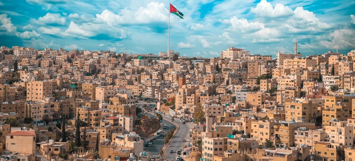 aerial image of Amman Jordan with blue skies, the large country flag, and many adobe houses 