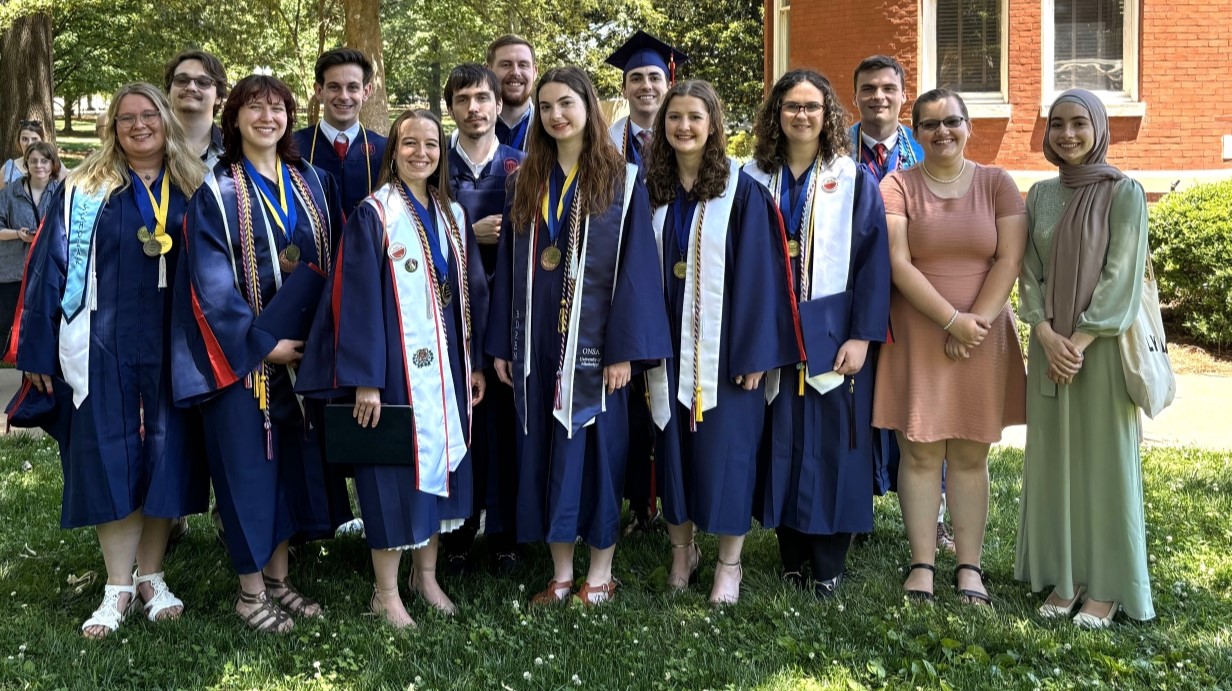 image of a group of students in graduation caps and gowns standing together for a photo on UM campus