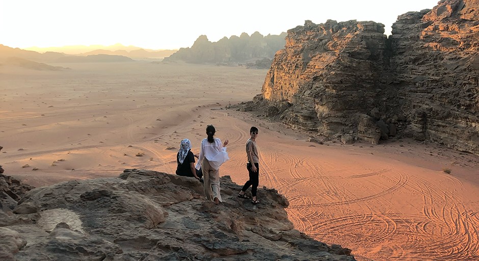 a few students standing on a rocky outcropping within a desert mountains landscape