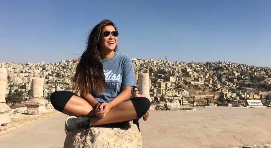 student seated crosslegged with the desert city of Amman in the background