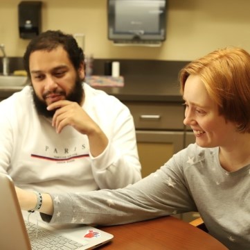 image of two students seated together at a table and looking at laptop computer screen