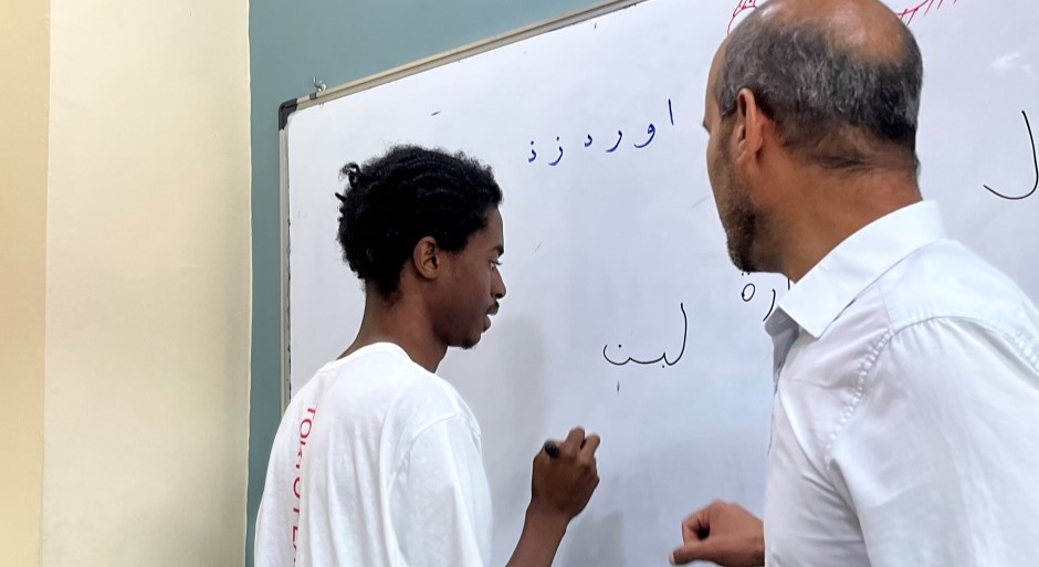 student and a teacher at a whiteboard drawing Arabic calligraphy