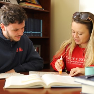 image of two students seated together at a table and looking at the papers on the table