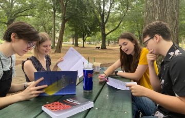 a group of students seated together at a picnic table in the Grove studying