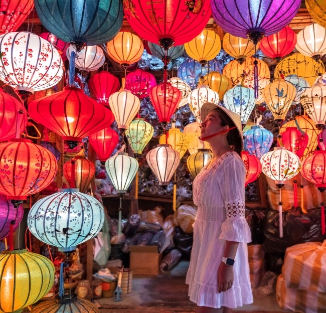 a woman is standing and looking up a colorful lit lanterns 