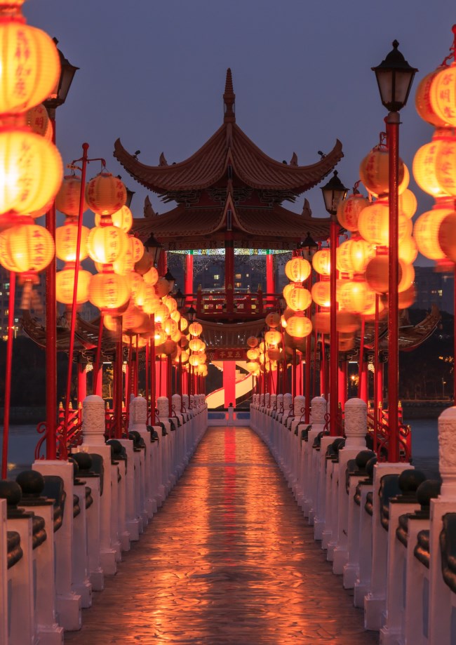 image of Chinese lanterns lining a walkway to a traditional pagoda on a lake.