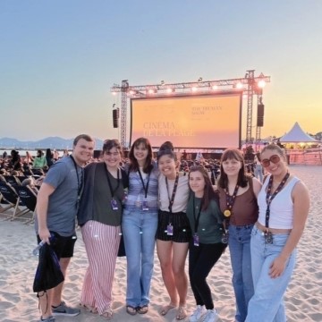 students stand together on a beach with a temporary movie screen behind them