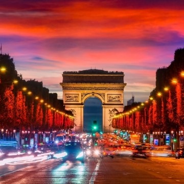 road toward an arch in the twilight with trees lit in red light