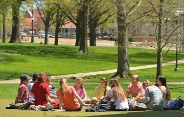 a small group of students sitting in a circle outside in a park-like setting