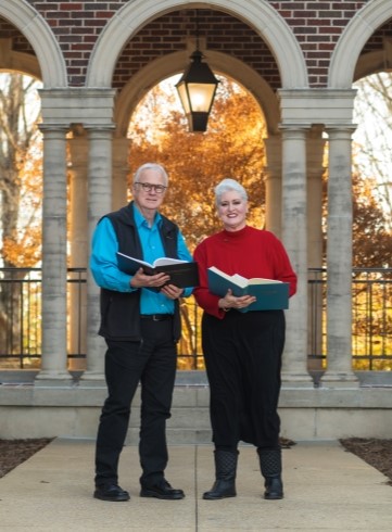 Dr. Michael Raines and Dr. Felice Coles standing together outside in front of a building. Both are holding books