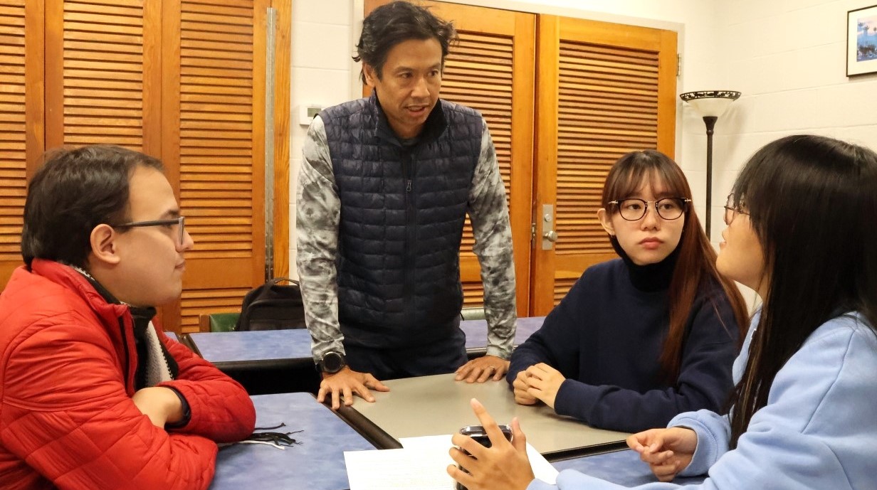 image of several students around a table with a professor standing and talking with them